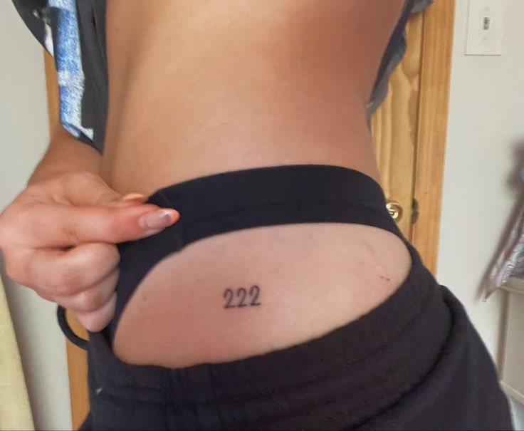 a woman with a small tattoo on her lower back and the number 22 written in cursive writing