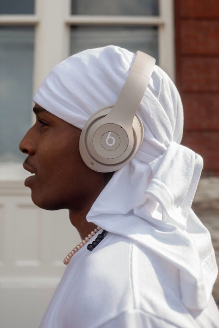 a man wearing headphones and a white dress is standing in front of a brick building