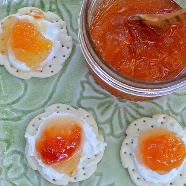 three small crackers with jam on them next to a jar of jelly and spoon