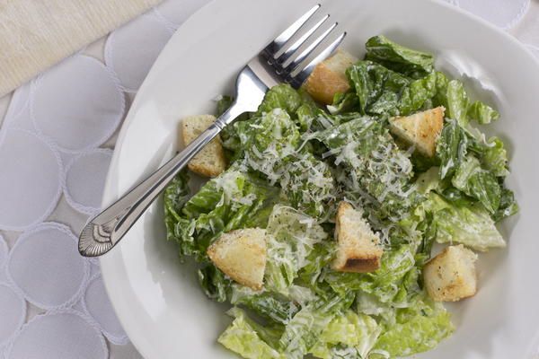 a white bowl filled with lettuce next to a fork and knife on top of a table