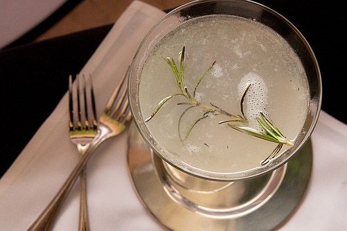 a silver plate topped with a glass filled with ice and garnished with rosemary