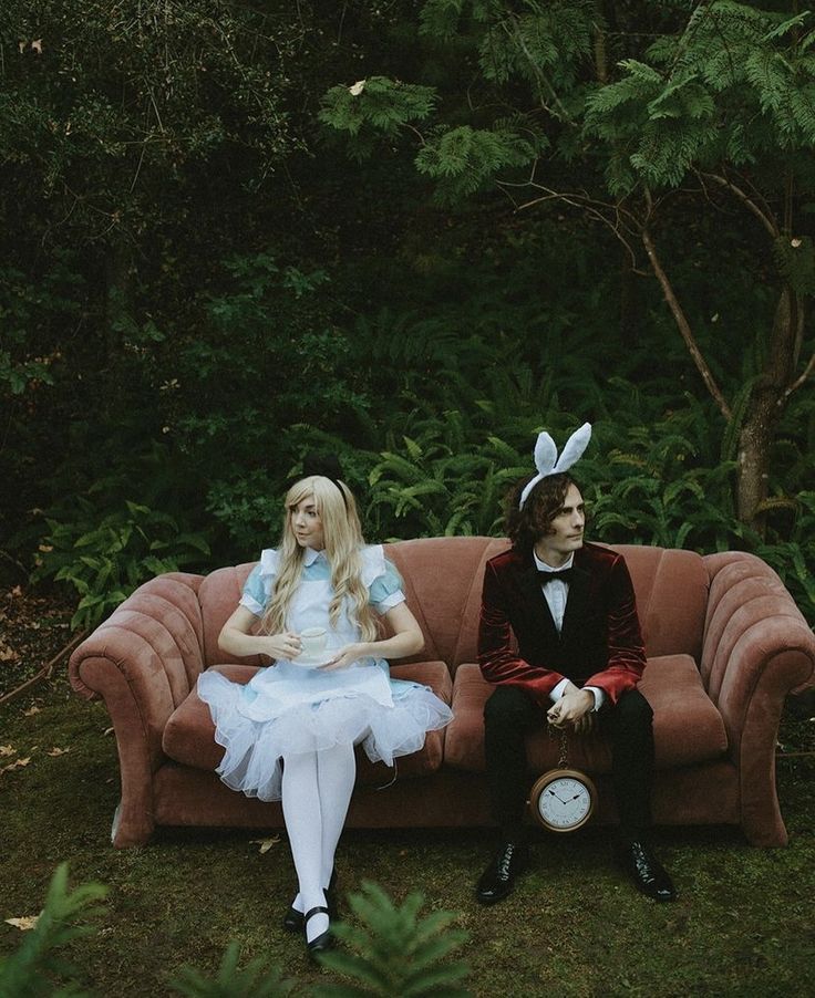 two people dressed up as alice and the rabbit sitting on a couch in front of some trees