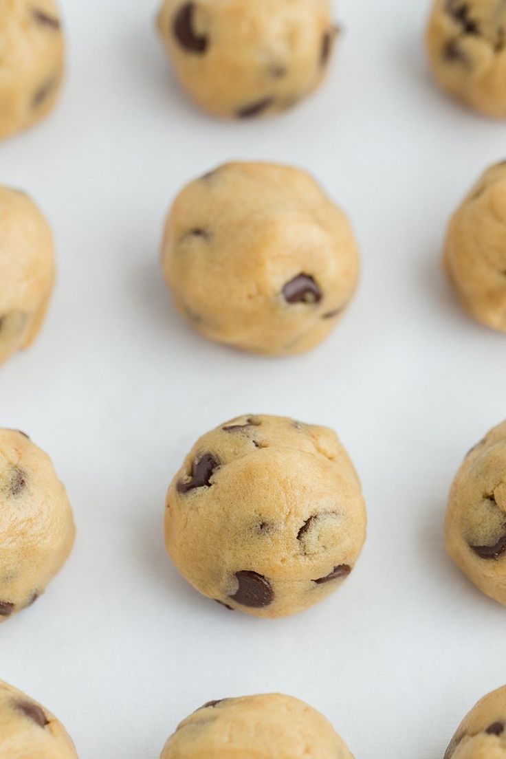 many chocolate chip cookies are lined up on a white surface and ready to be baked