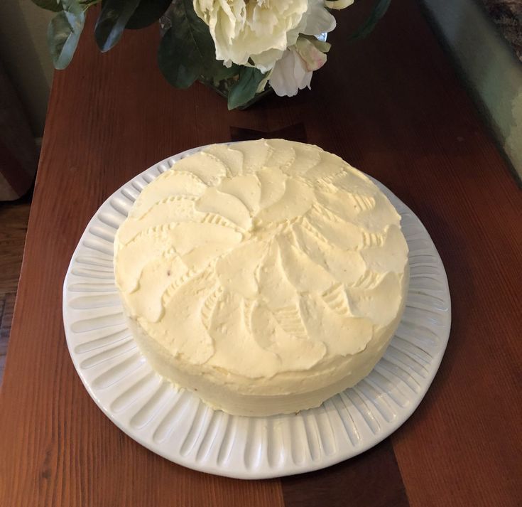 a white cake sitting on top of a wooden table next to a vase with flowers