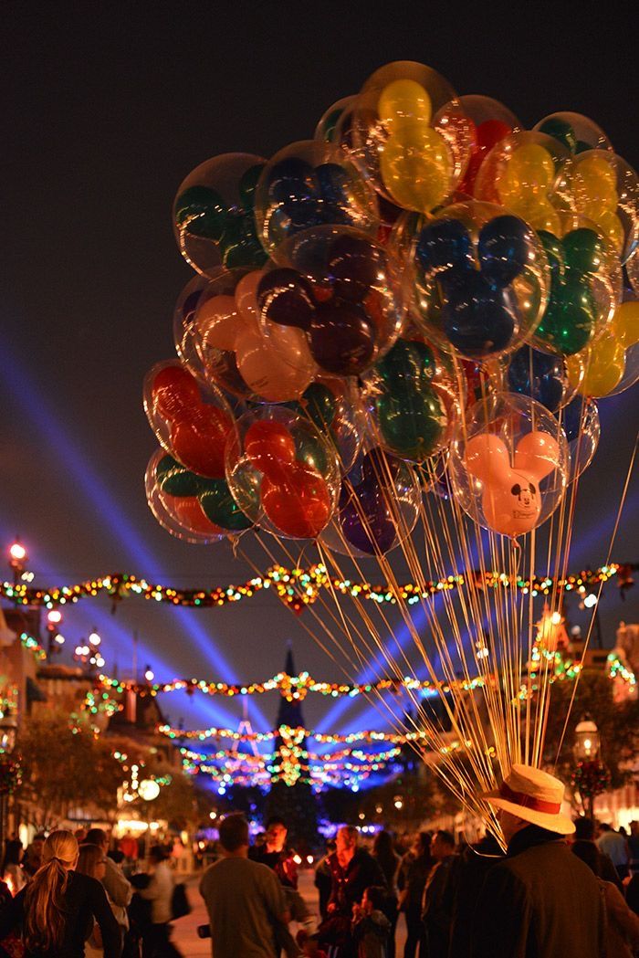 a bunch of balloons are floating in the air with lights on them and people walking around