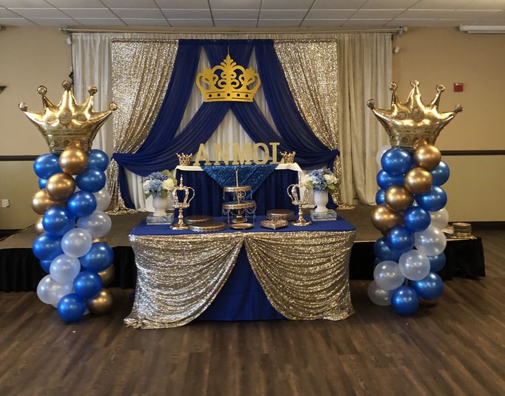 a table with blue and gold decorations on it, including two large balloons in the shape of crowns