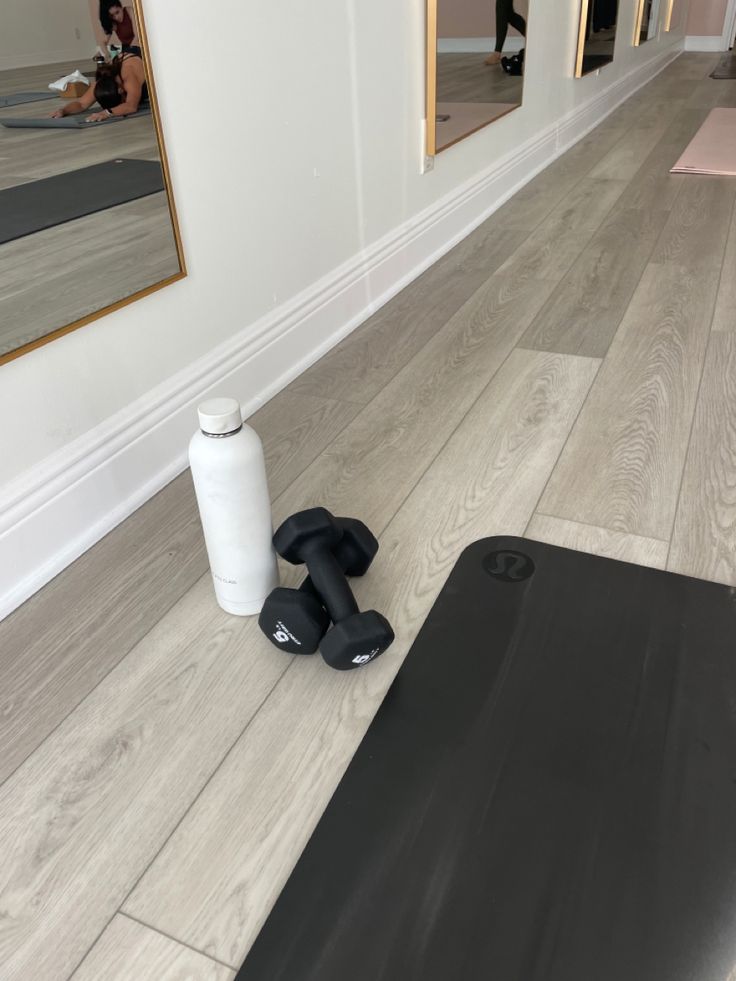 an exercise mat, water bottle and gym equipment on the floor in front of a mirror