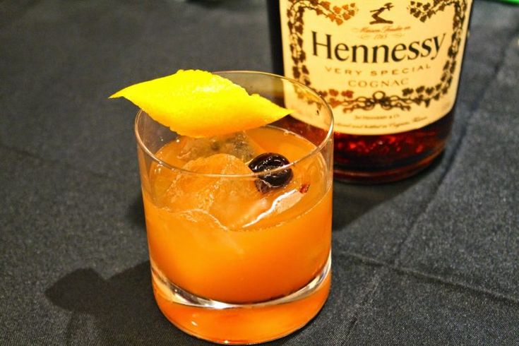 an orange drink in a glass next to a bottle of hennesby gin tonic