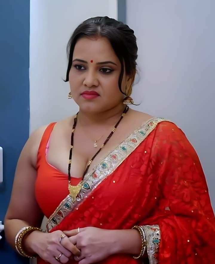 a woman in a red sari is looking at the camera while standing next to a blue wall