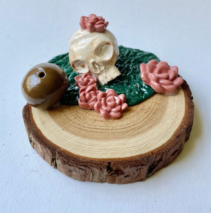 a small figurine is sitting on top of a piece of wood with flowers and a ball