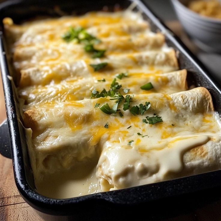 a casserole dish with cheese and green garnish in it on a wooden table