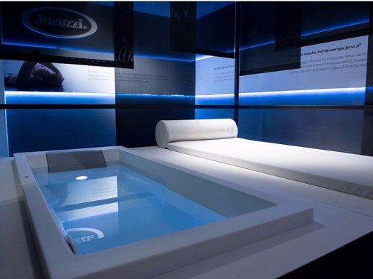 a bath tub sitting inside of a bathroom next to a white counter top under blue lights