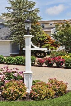 a white lamp post with flowers and bushes around it