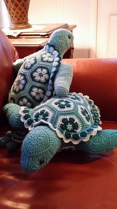 a crocheted turtle sitting on top of a brown couch next to a pillow