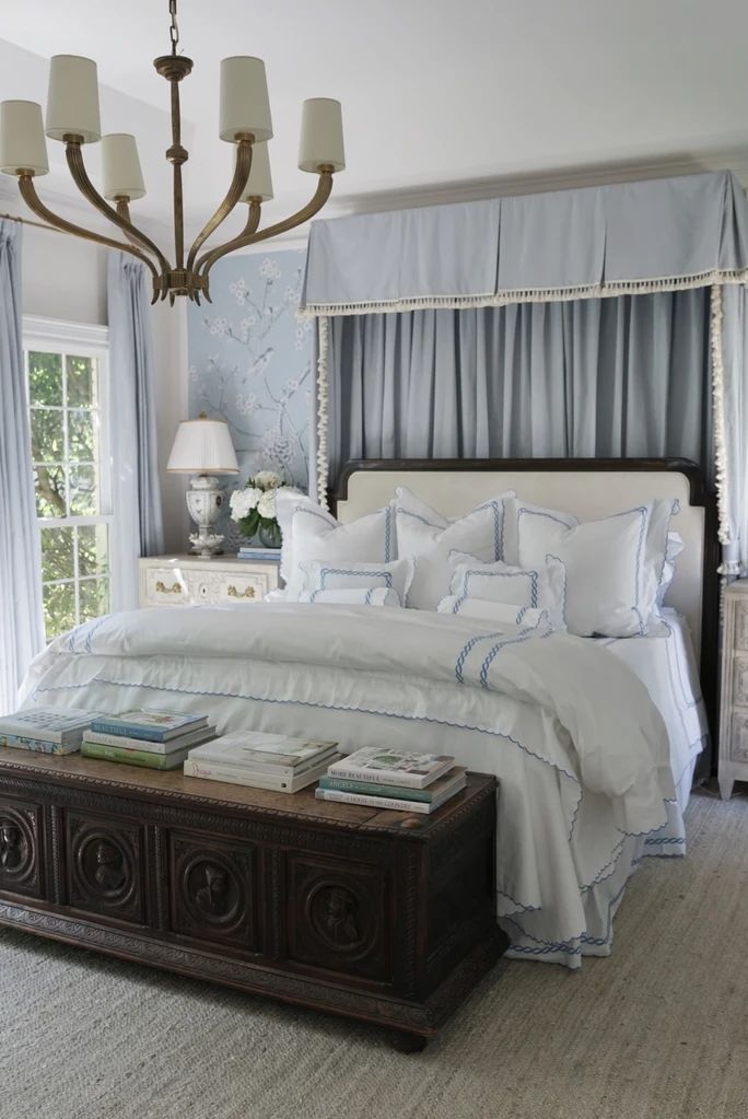 a white bed sitting under a chandelier in a bedroom next to a window