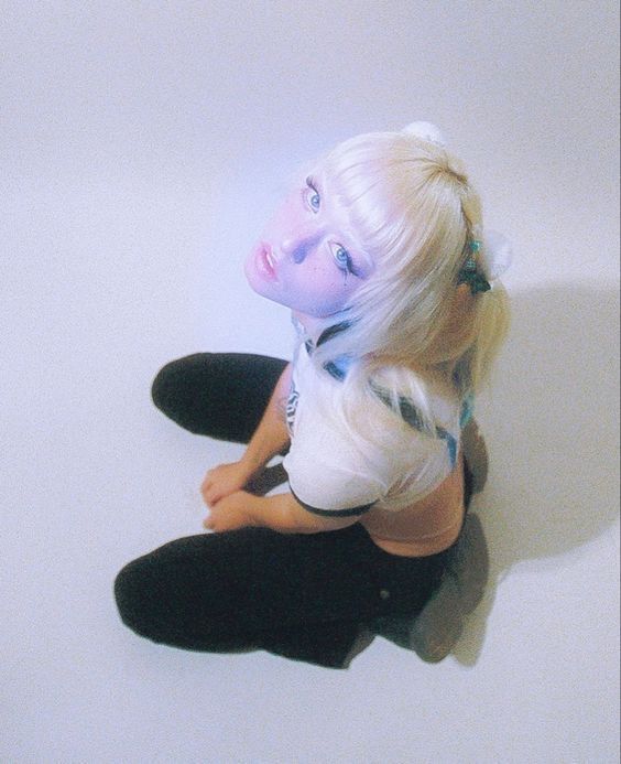 a woman with white hair and blue makeup sitting on the floor