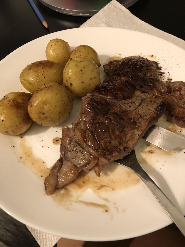 a white plate topped with meat, potatoes and gravy next to a knife