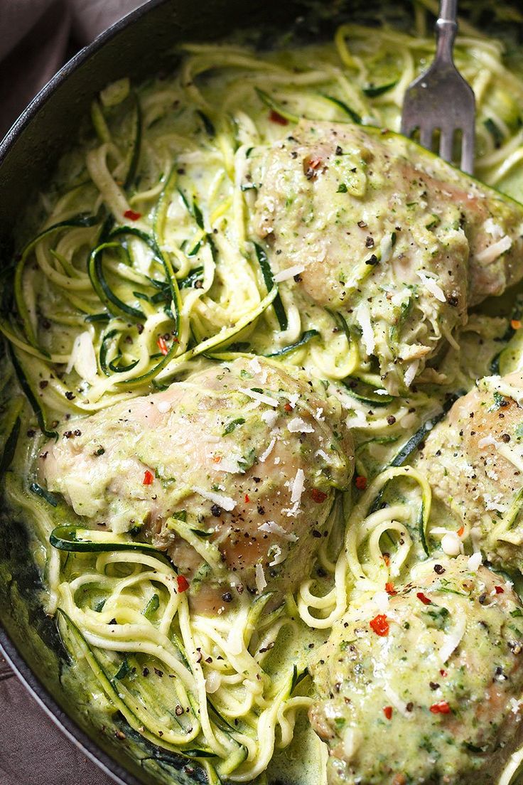 a skillet filled with pasta and meat covered in pesto sauce on top of a wooden table