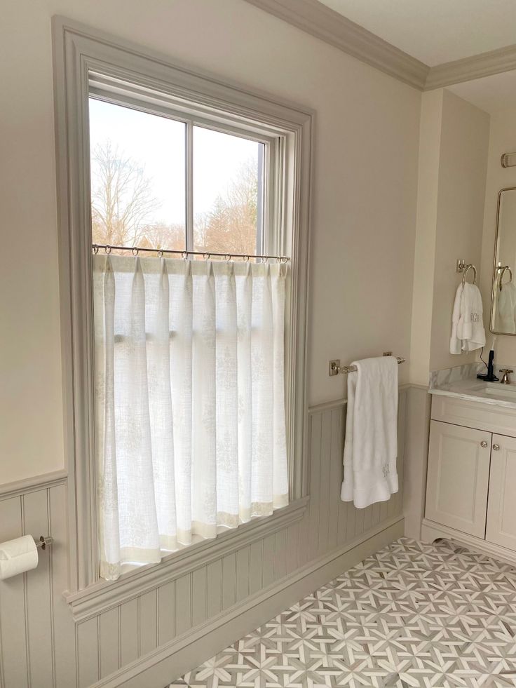 a bathroom with white walls and tile flooring next to a window that has curtains on it