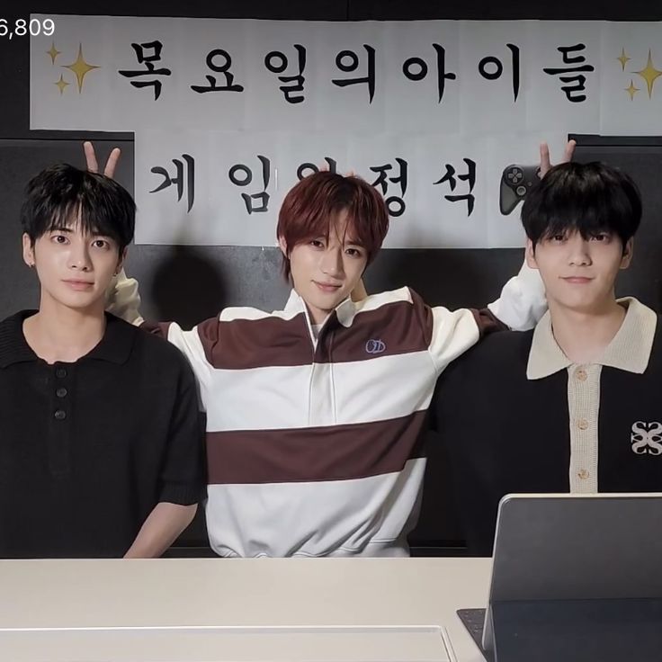 three young men standing next to each other in front of a laptop computer on a desk