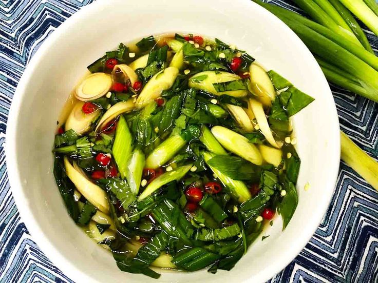 a white bowl filled with green vegetables on top of a blue and white table cloth