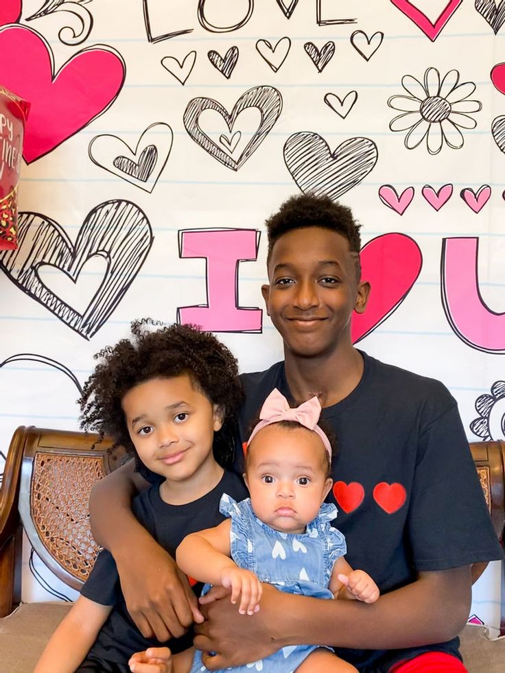 a man and woman holding a baby in front of a wall with hearts on it