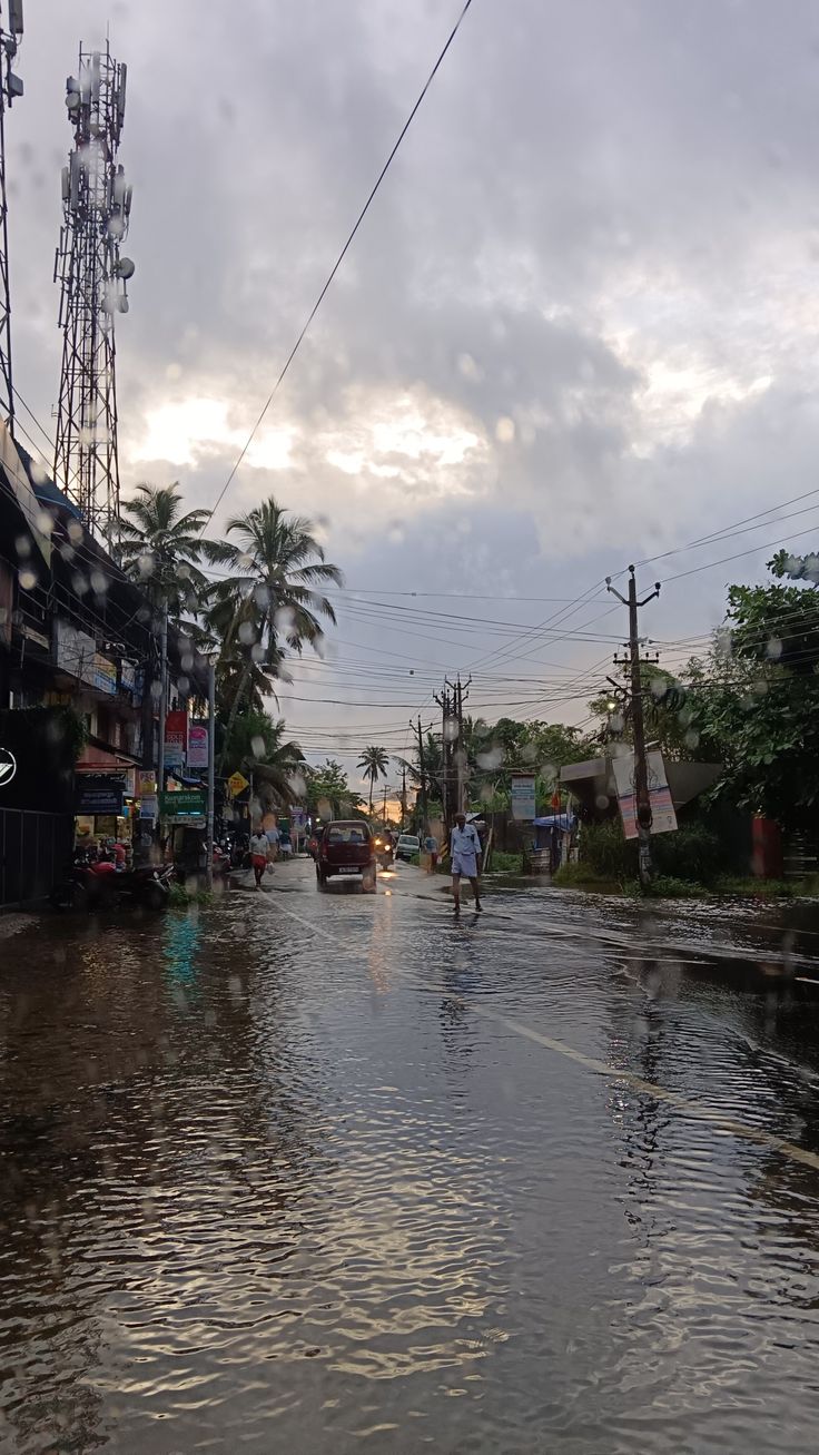 people are walking down the flooded street in front of shops and telephone poles on a cloudy day