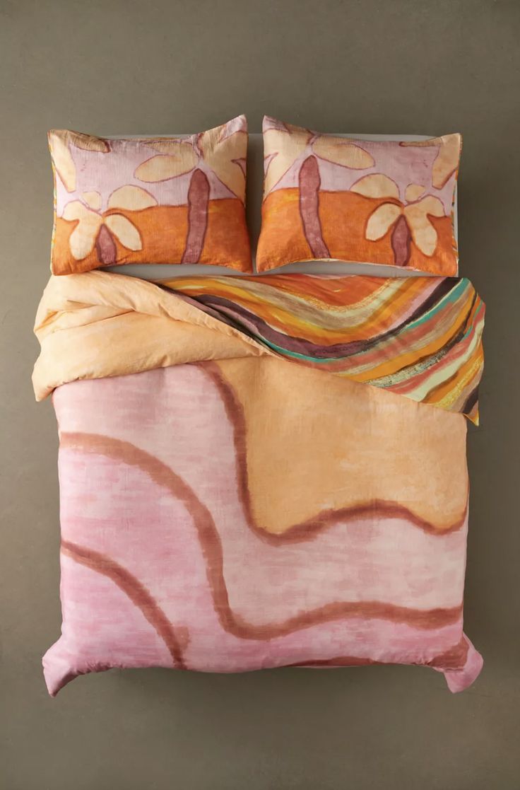 a bed with two pillows on top of it and an orange comforter in the middle