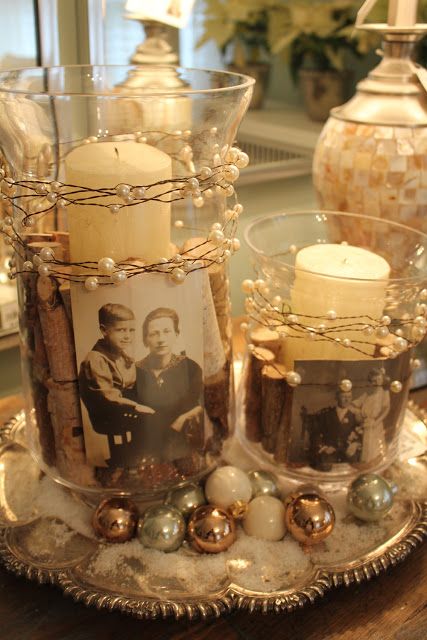 two glass vases filled with candles sitting on top of a table next to pictures