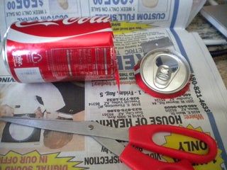 a can of soda and scissors on top of newspaper