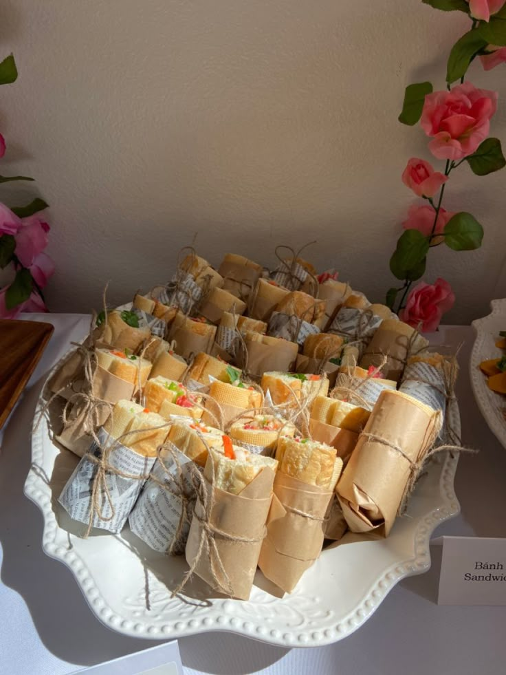 a platter filled with sandwiches on top of a table next to other plates and flowers