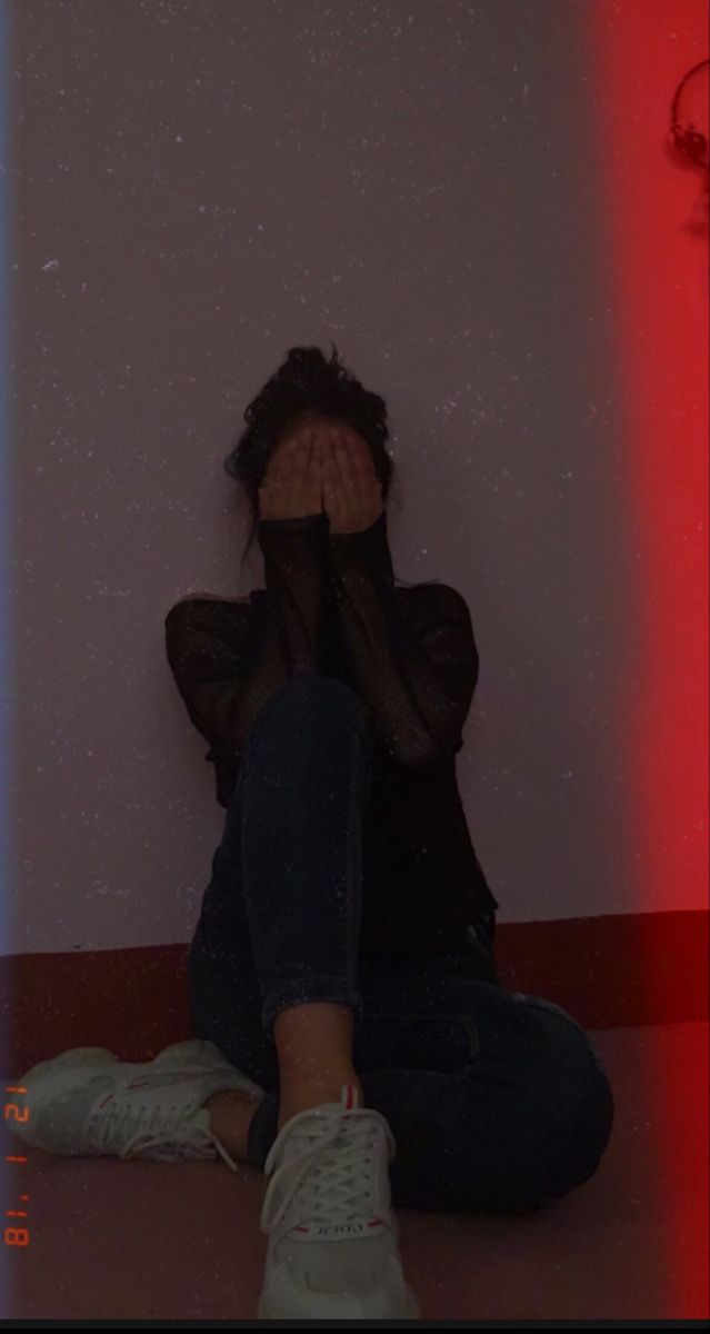 a woman sitting on the floor covering her face with her hands, in front of a red and blue light