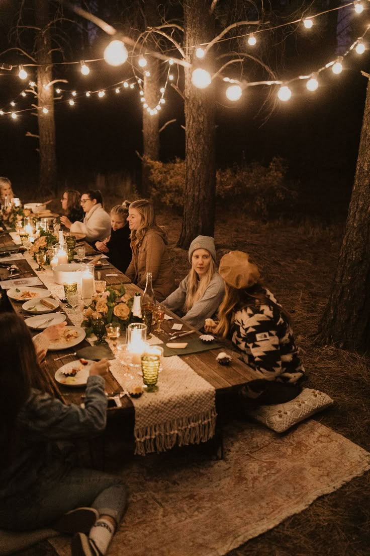 a group of people sitting around a table with food and drinks on it at night