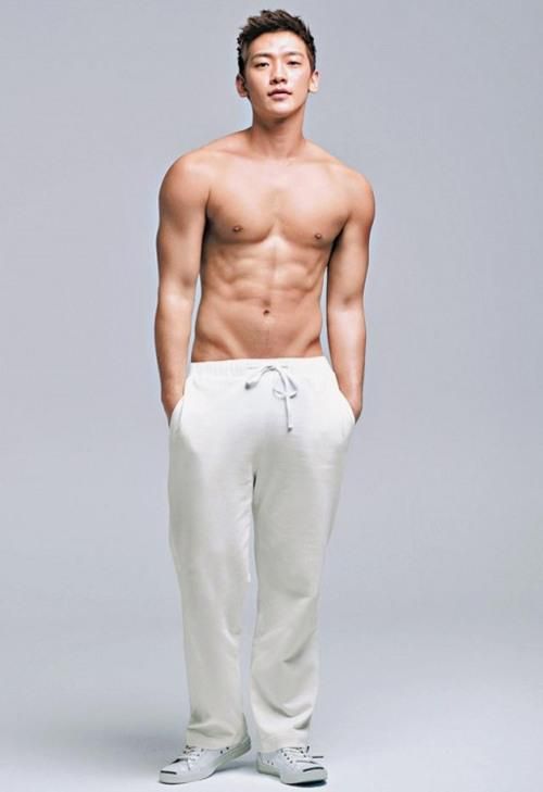 a man with no shirt standing in front of a gray background wearing white sweatpants