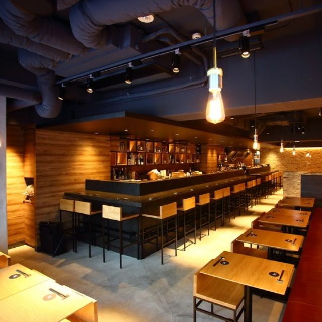 an empty restaurant with wooden tables and black counter tops is lit by light bulbs hanging from the ceiling