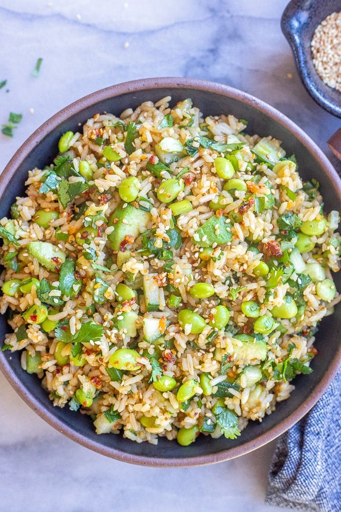 a bowl filled with rice and vegetables on top of a marble table next to a spoon