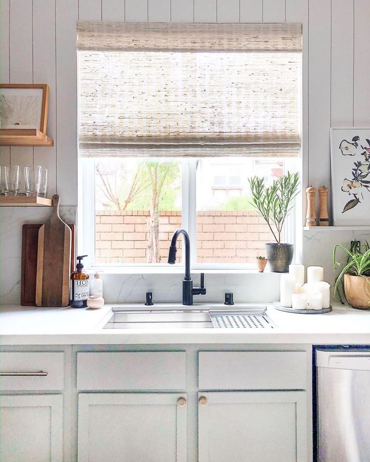 a kitchen with white cabinets and countertops has plants on the window sill in front of the sink