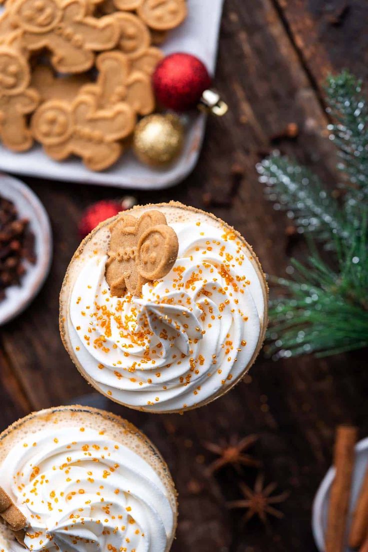 two glasses of hot chocolate with whipped cream and ginger cookies on the side, surrounded by christmas decorations