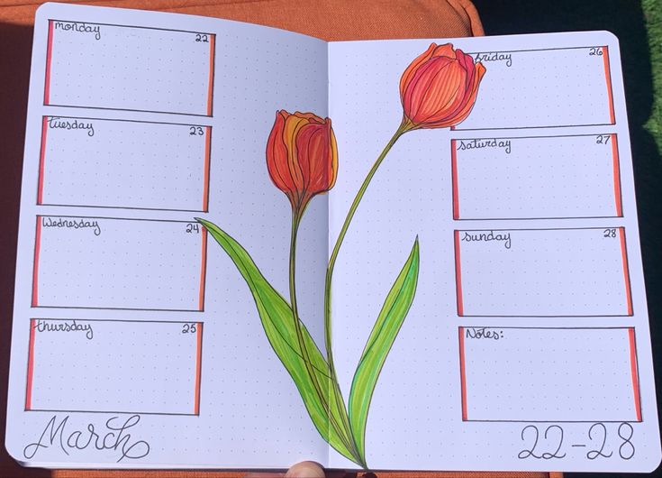 a hand holding an open planner with two flowers on it