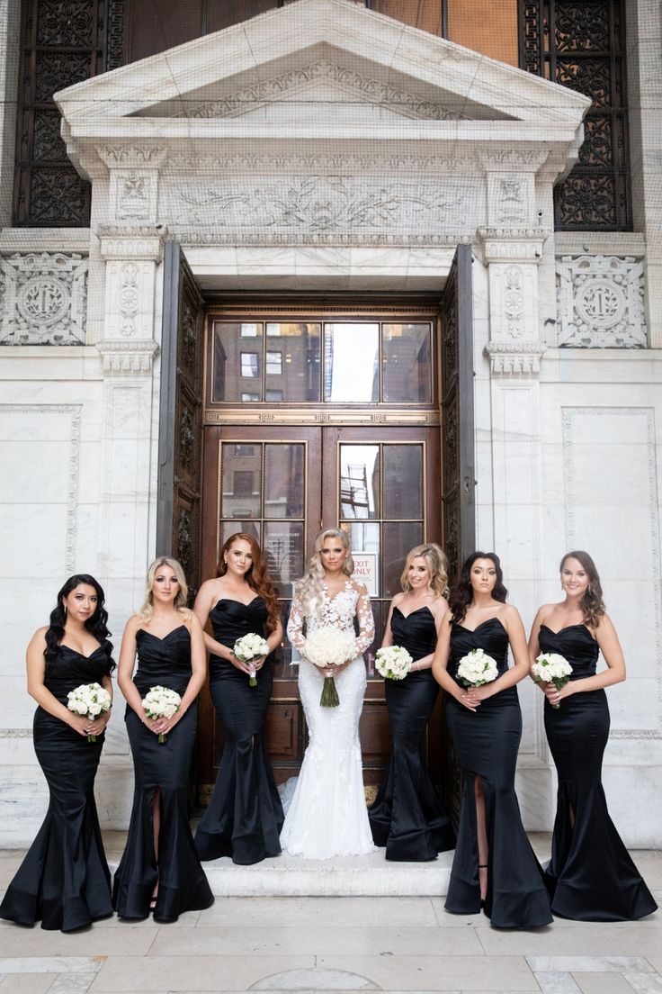 a group of women standing next to each other in front of a door wearing black dresses