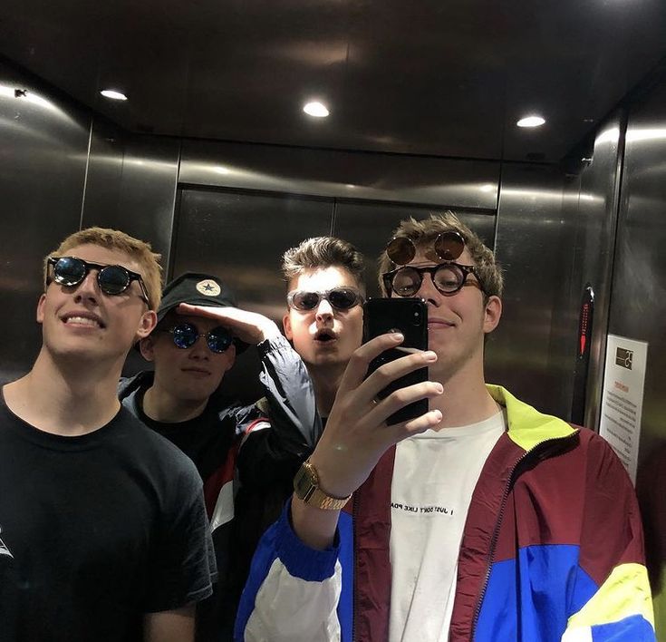 a group of young men standing next to each other in front of a mirror taking a selfie