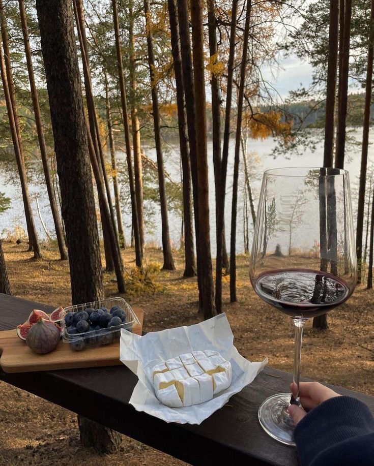 a person sitting at a picnic table with food and wine in front of the lake