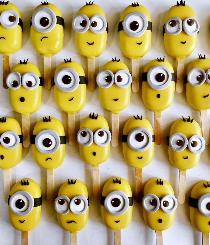 minion lollipops with googly eyes are arranged on wooden skewers