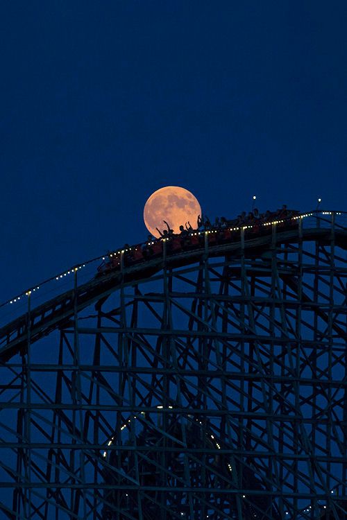 a full moon is seen over the top of a roller coaster