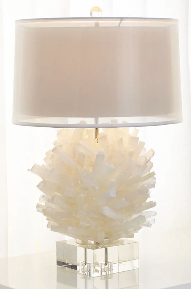 a lamp that is on top of a table with a glass base and white lampshade