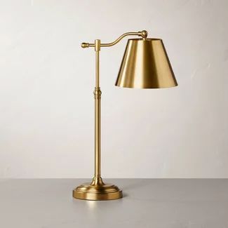 a gold lamp on a table with a white wall in the backgrounnd