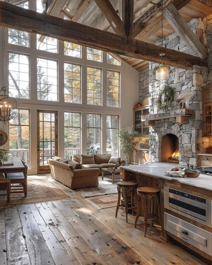 a large open concept kitchen and living room with wood flooring, stone walls, exposed beams, and windows