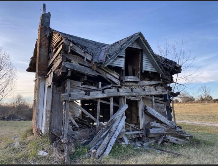 an old run down wooden house in the middle of a field with grass and trees