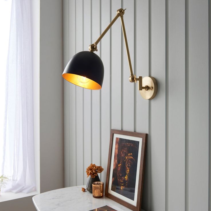 a black and gold wall light next to a white table with a framed photograph on it