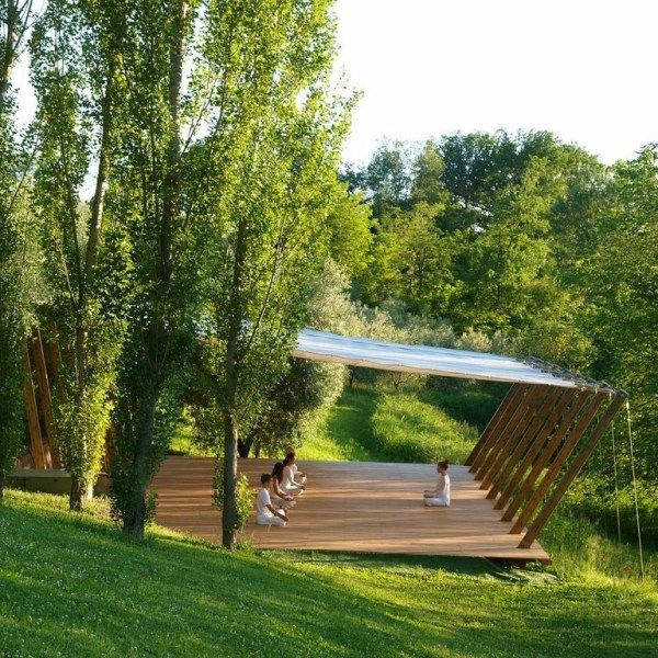 two people sitting on a wooden platform in the middle of a park with green grass and trees